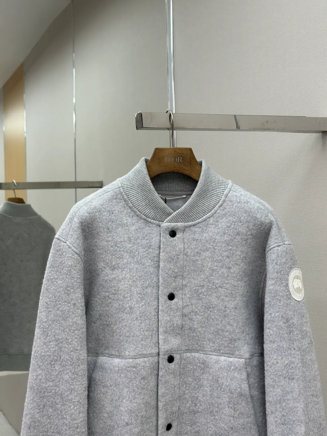 P770 Canada Goose Fleece Badge Button Jacket Fabric selection: Wool blend fabric: The main fabric of this jacket is light gray wool blend fabric to improve the fabric's wear resistance, wrinkle resistance and warmth. Wool provides good warmth and a natural feel, while blended fibers enhance the fabric's practicality and durability.  RIBBED KNIT: The collar, cuffs and hem are ribbed knitted for added stretch and fit.  Production process: The cutting process needs to ensure that the texture and color of the fabric are evenly distributed, especially for this light gray tone, to avoid color differences. The stretchability of wool-blend fabrics needs to be taken into consideration when cutting pieces to ensure dimensional stability of the finished garment.      • Use a sewing needle and thread suitable for wool-blend fabrics to avoid damage to the fabric during sewing. The sewing stitches are even and firm to prevent thread stripping.      • The temperature needs to be controlled during ironing to avoid high temperature damage to the fabric while keeping the fabric smooth and crisp.  Main body splicing: • The front and back body parts, sleeves and other main parts are spliced ​​with flat seams to ensure a smooth silhouette. •Align the fabric texture at the splicing points to keep the appearance neat.     Details such as pockets and cuffs are designed with inset pockets to increase practicality and aesthetics.     The splicing areas are reinforced to improve durability.  Armband: The white round armband on the left arm is an important part of the brand identity and is finely sewn to ensure it is strong and flat.  Dark gray and light gray Size: S M L XL